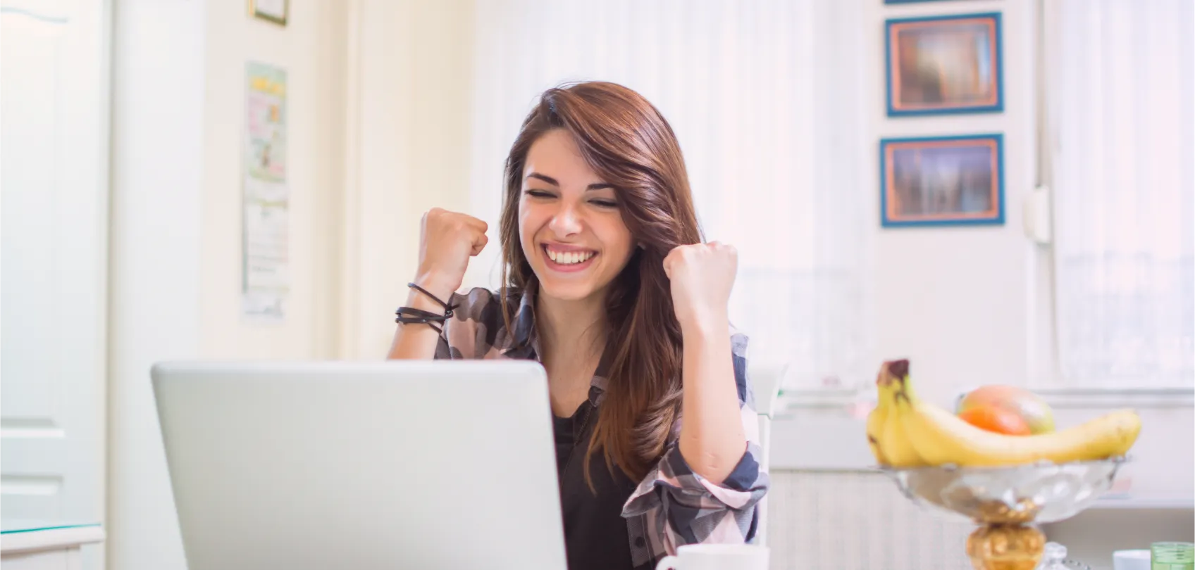 Mujer joven sonriente celebrando frente a su computadora portátil, simbolizando el éxito de tener un sitio web inteligente que trabaja para el negocio.