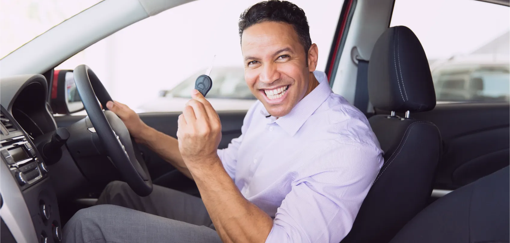 Cliente feliz sentado en su nuevo automóvil, mostrando la llave con una sonrisa de satisfacción