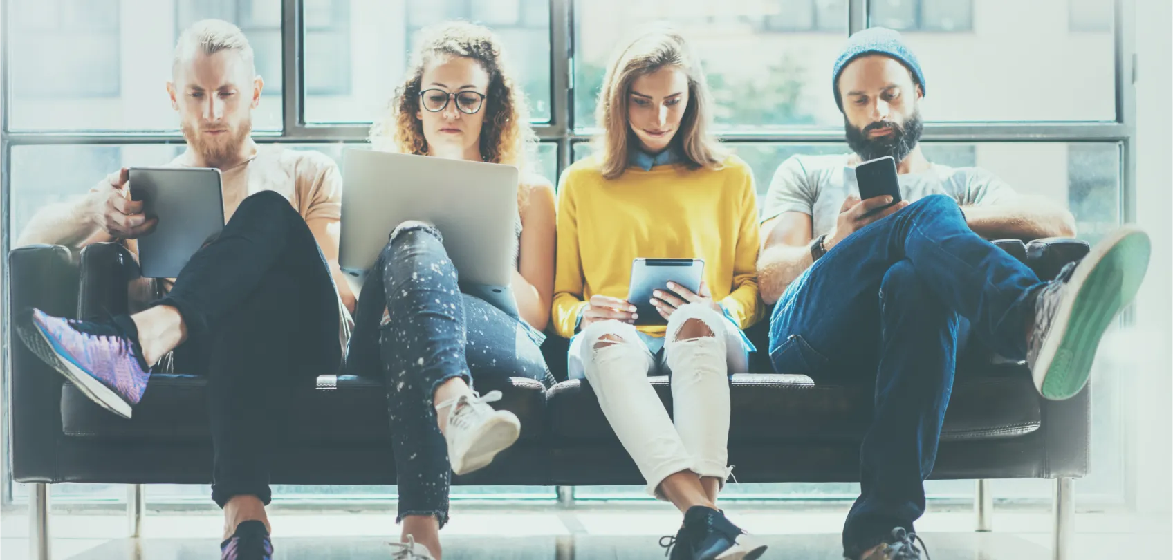 Cuatro jóvenes sentados en un sofá, cada uno usando un dispositivo en un espacio luminoso, representando el uso de tecnología y datos en marketing.