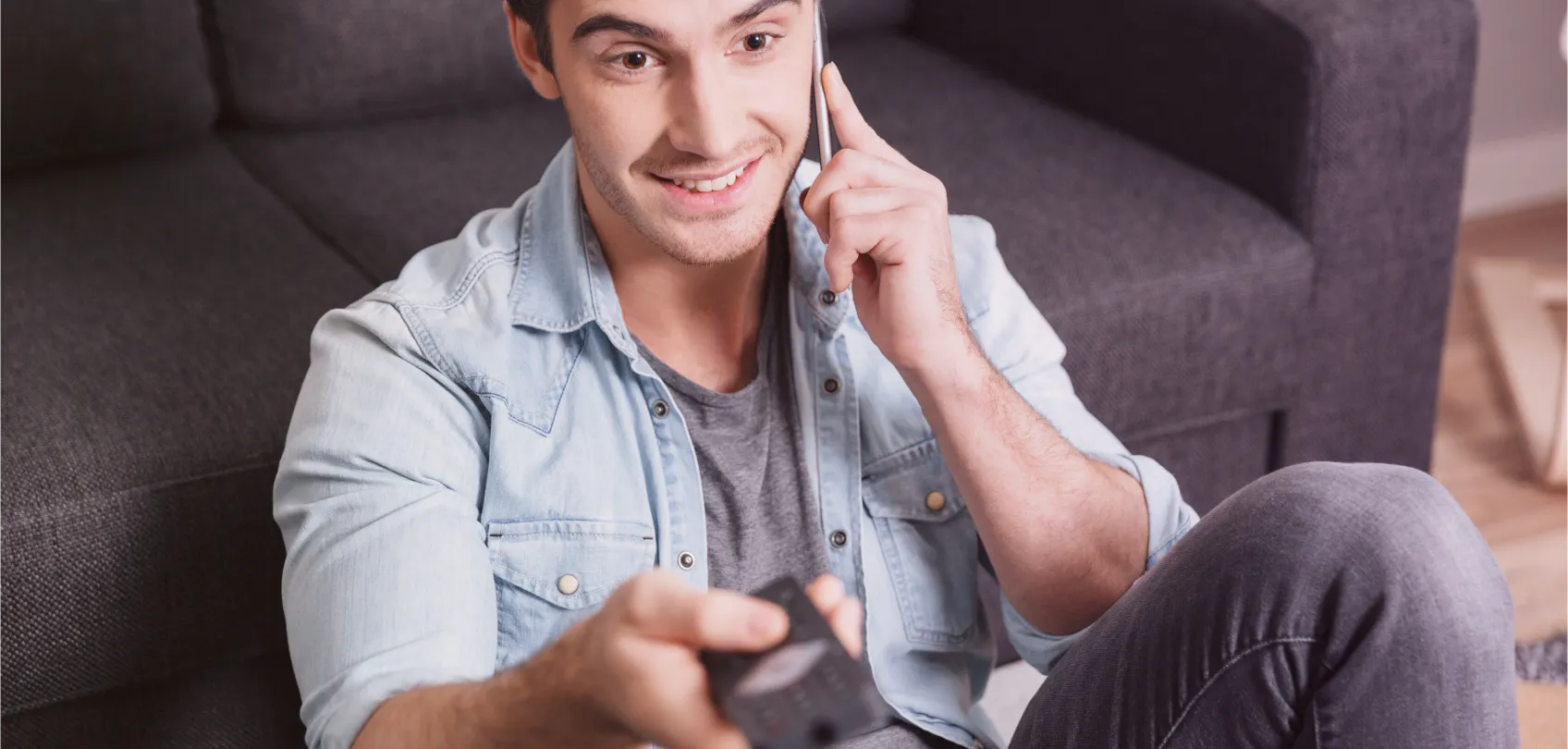 Joven sonriendo mientras habla por teléfono y sostiene un control remoto, representando múltiples canales de comunicación en una experiencia omnicanal.