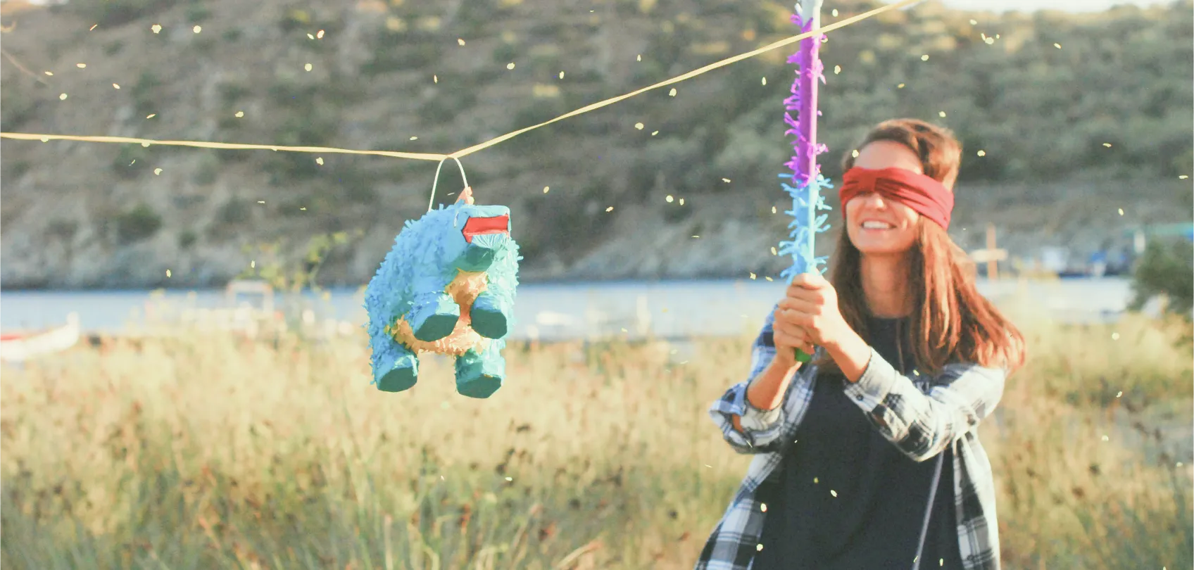 Mujer con los ojos vendados intenta golpear una piñata azul en un campo abierto, representando la metáfora de trabajar a ciegas.